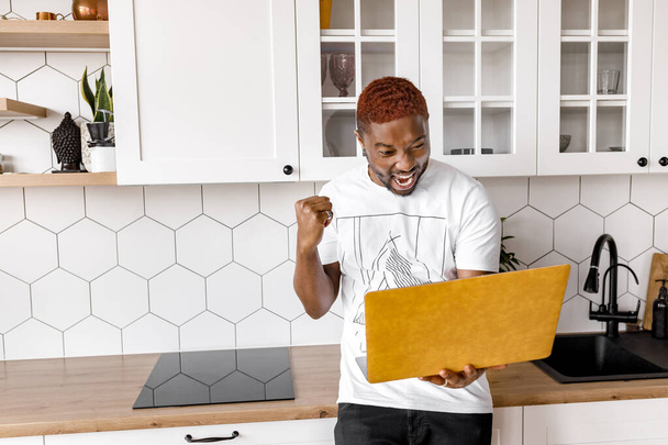 african american man with laptop  in kitchen - Фото, изображение