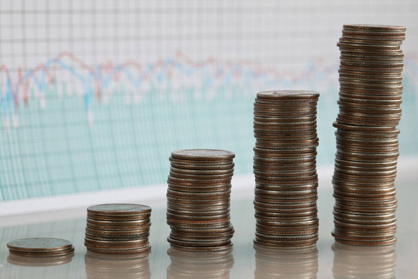 Stapels munten die in rijen toenemen tegen de achtergrond van financiële indicatoren - Foto, afbeelding
