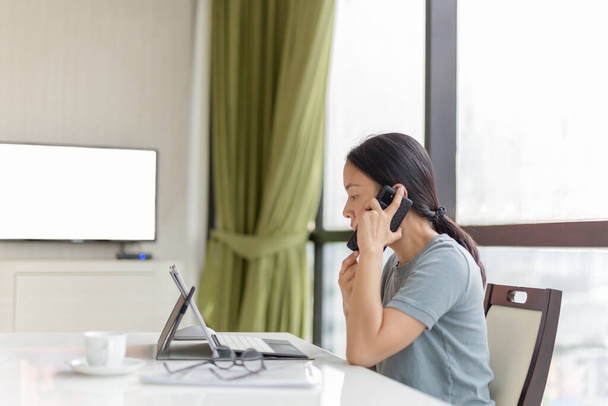 Mujer de negocios hablando por teléfono celular mientras trabaja en el portátil. - Foto, Imagen