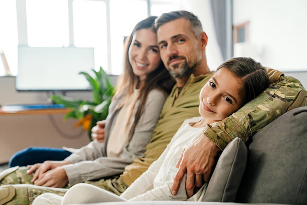 Happy masculine military man hugging his family while sitting on sofa indoors - Foto, afbeelding