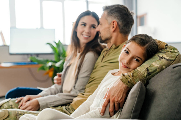 Happy masculine military man hugging his family while sitting on sofa indoors - Foto, Imagem