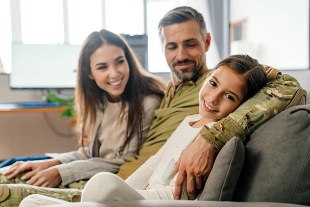 Happy masculine military man hugging his family while sitting on sofa indoors - Фото, зображення