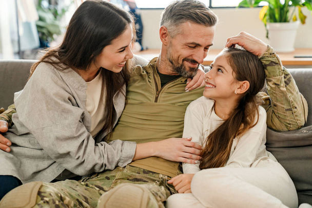 Felice uomo militare maschile abbracciare la sua famiglia mentre seduto sul divano in casa - Foto, immagini