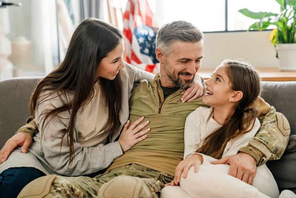 Happy masculine military man hugging his family while sitting on sofa indoors - Foto, immagini