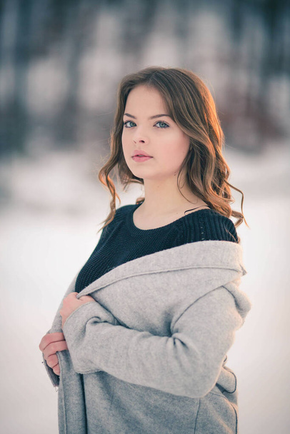 A shallow focus of a brunette woman wearing a cardigan with a sweater and posing in a forest in winter - Fotó, kép