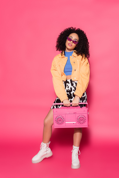 full length of african american woman holding retro boombox on pink  - Foto, Imagem