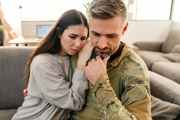 Szomorú fiatal katona elbúcsúzik a szomorú feleségétől otthon. - Fotó, kép