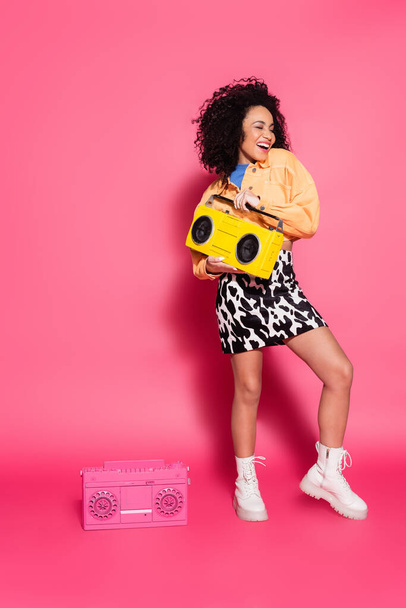 full length of cheerful african american woman holding yellow boombox on pink - Photo, Image