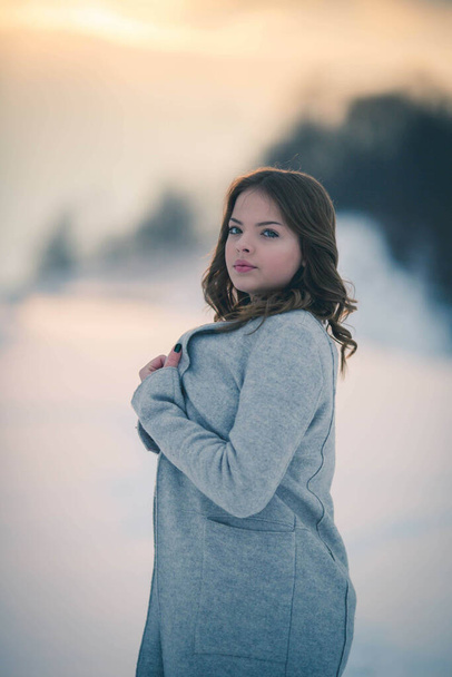 A shallow focus of a young woman wearing a gray coat and posing in a forest covered in the snow - Fotó, kép