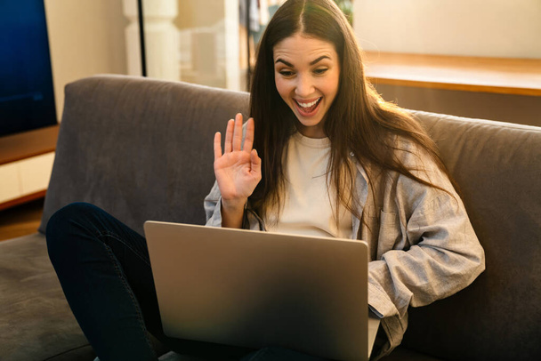 Happy young attractive woman looking at laptop screen, waving hands, on a video call with friends from home - Φωτογραφία, εικόνα