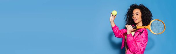 curly african american woman holding tennis ball and racket on blue, banner - Foto, Bild