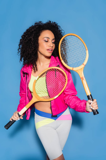 young african american woman holding tennis rackets on blue - Фото, изображение