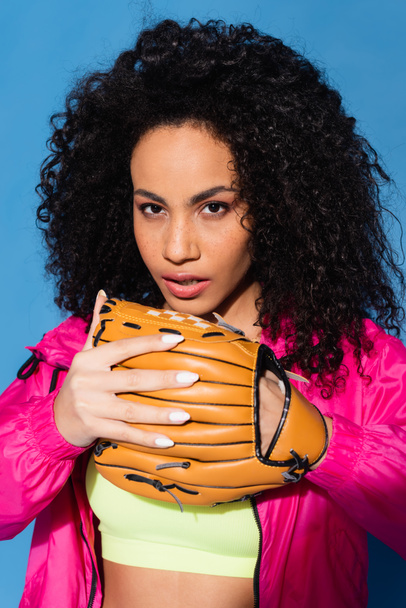 sporty african american woman wearing leather baseball glove isolated on blue - Foto, imagen