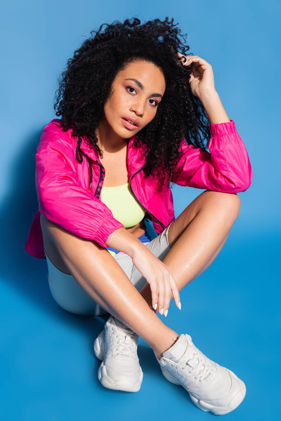 curly african american woman in pink jacket sitting on blue - Foto, Bild