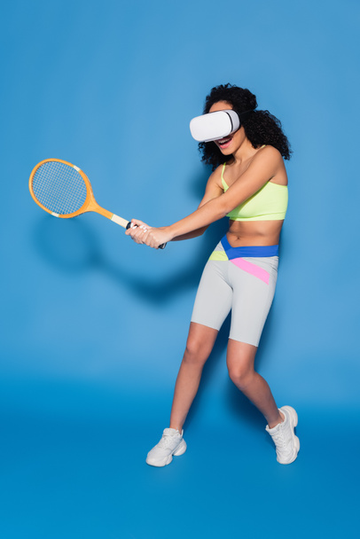full length of african american woman in vr headset playing tennis on blue - Foto, Imagem