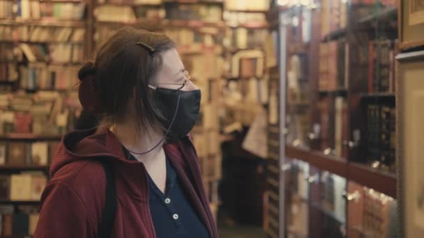 Γυναίκα με γυαλιά και μάσκα κατά του ιού επιλέγει ζωγραφική για να αγοράσει σε κατάστημα με αντίκες - Πλάνα, βίντεο