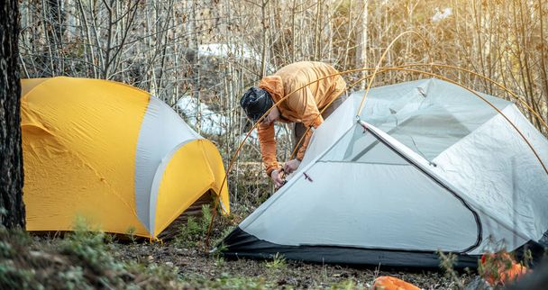 Bir erkek yürüyüşçü ormanda bir çadır kuruyor. Turizm, yürüyüş ve doğada kalma kavramı. - Fotoğraf, Görsel