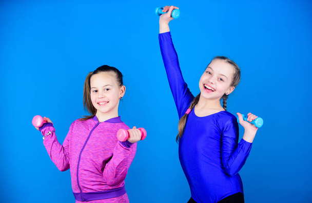 Girls exercising with dumbbells. Beginner dumbbells exercises. Children hold dumbbells blue background. Sport for teens. Easy exercises with dumbbell. Sporty upbringing. On way to stronger body - Fotó, kép