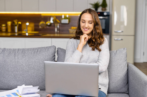 Happy woman sits on the comfortable sofa with a laptop on the laps - Foto, immagini