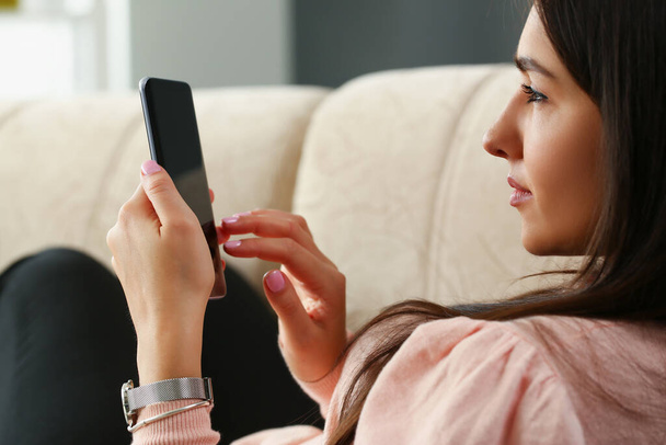Lonely woman is sitting on couch and looking into smartphone - Photo, Image