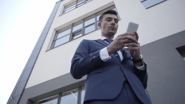 Niedriger Blickwinkel auf Geschäftsmann, der Smartphone draußen benutzt - Filmmaterial, Video