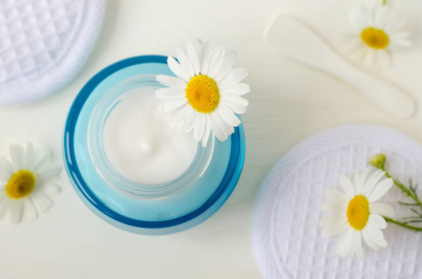 White facial mask (face cream, hair mask, body butter, facial cleanser) in the small blue jar and chamomile flower. Natural skin and hair treatment concept. Top view, copy space. - Photo, Image