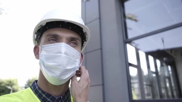 Οικοδόμος σε σκληρό καπέλο απογειώνεται ιατρική μάσκα σε εξωτερικούς χώρους - Πλάνα, βίντεο