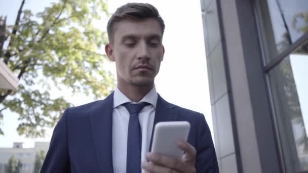 Бизнесмен использует смартфон и улыбается на открытом воздухе  - Кадры, видео