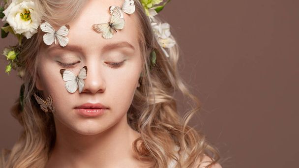 Beautiful blonde woman face with healthy hair, clear skin, white spring flowers and butterfly on brown background closeup portrait - Photo, Image