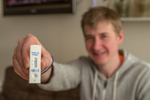 Nuori onnellinen hymyilevä valkoihoinen mies pitää kädessään koronaviruksen pikatestiä Self Express Coronavirus Test kotona, nuori mies testattu negatiiviseksi covid-19 pikatestillä.  - Valokuva, kuva