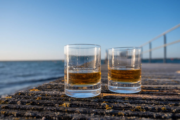 Picie whisky single malt Scotch whisky o zachodzie słońca z widokiem na morze, ocean lub rzekę, prywatne wycieczki po gorzelniach whisky w Szkocji, Wielka Brytania - Zdjęcie, obraz