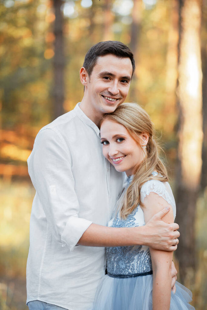 Счастливая молодая пара на вечерней прогулке в лесу и у озера. На невесте голубое свадебное платье.. - Фото, изображение