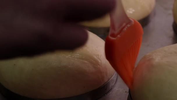 Process of making round bread. Baker applying yolks on raw dough with pastry brush. Close up - Footage, Video