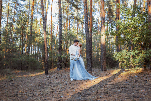 Счастливая молодая пара на вечерней прогулке в лесу и у озера. На невесте голубое свадебное платье.. - Фото, изображение