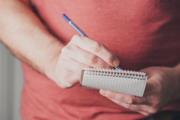 чоловік робить нотатки на маленькому спіральному блокноті, використовуючи олівець
 - Фото, зображення