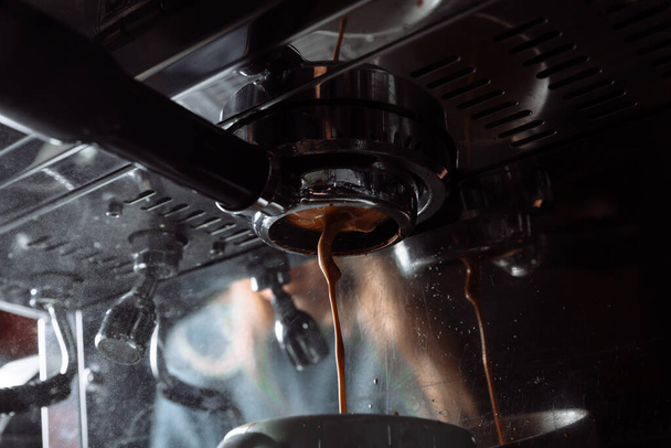 Kawa espresso przelewa się z automatu do białego kubka . - Zdjęcie, obraz