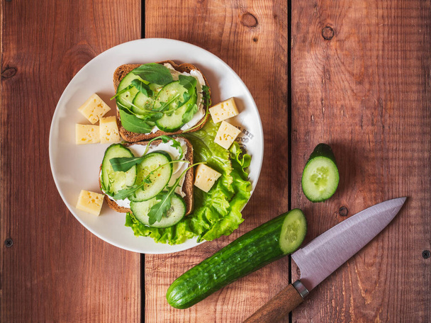 Sandwiches con croissants de queso y hierbas en platos blancos sobre la mesa, puesta plana, pepino y cuchillo de cocina - Foto, imagen
