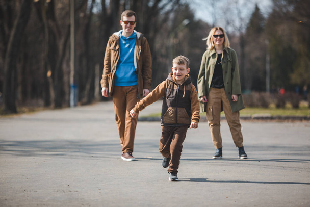 Şehir parkında küçük aktif bir çocukla genç ve sevimli bir aile. Etrafta koşuşturmak. sonbahar sezonu - Fotoğraf, Görsel