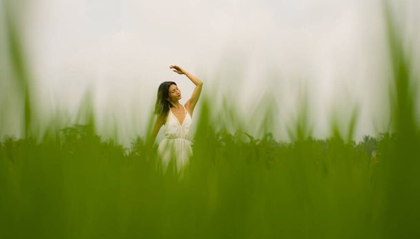 artistic portrait of young attractive and happy Asian woman outdoors at green rice field landscape wearing elegant long dress dancing on beautiful nature carefree  - Photo, Image