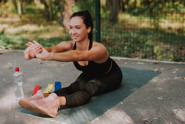 Young woman in black sportswear stretching and doing sport in park. Attractive fit girl doing yoga. Healthy lifestyle concept. - Photo, Image
