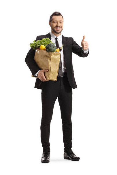 Full length portrait of a businessman carrying a grocery bag and showing thumbs up isolated on white background - Foto, afbeelding