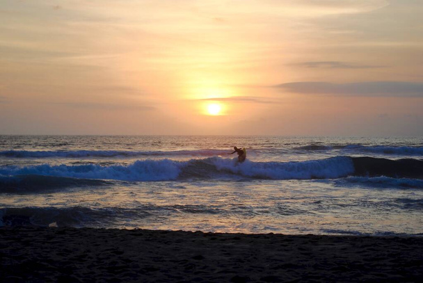 Сёрфер на закате. Пляж Фазан, Пантай, Бали, Индонезия. Бали - популярное место для серфинга со многими школами серфинга. Рядом с Кутой и Семиньяком.  - Фото, изображение