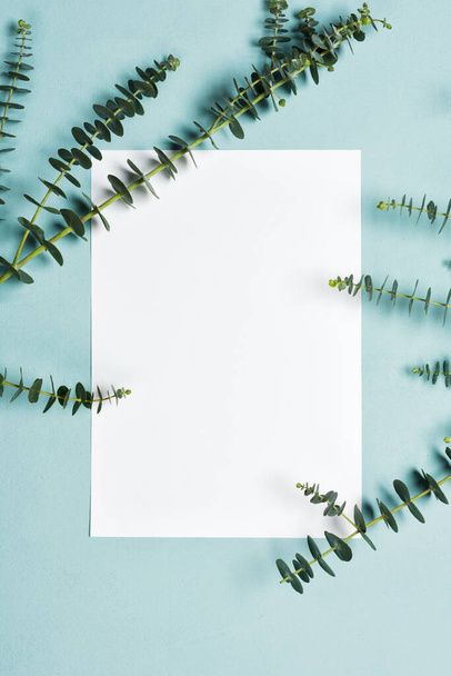 Einladungskarten-Attrappe mit Eukalyptuszweigen auf blauem Hintergrund - Foto, Bild