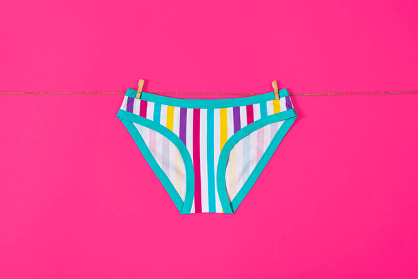Womens colorful striped panties hang on a rope. Girls underpants isolated on pink background, - Photo, Image