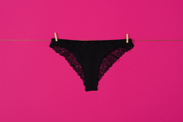 Womens black lace panties hanging on a rope. Girls underpants isolated on pink background. - Photo, Image