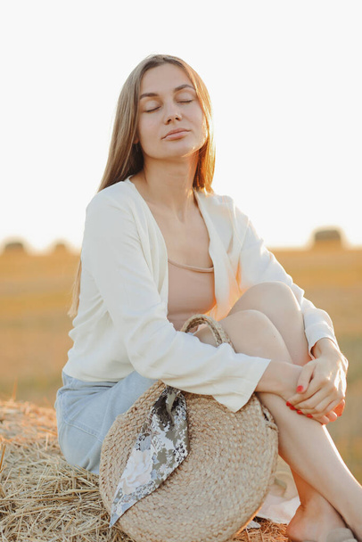 Gyönyörű portré egy fiatal nőről naplementekor, meleg sárga napsugarakkal az arcán, szalmabálákkal a háttérben.. - Fotó, kép