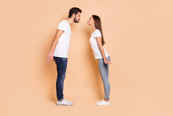 Full length photo of charming husband wife wear white t-shirts denim shoes ready to kiss isolated beige color background - Photo, Image