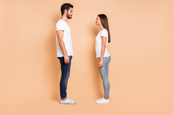 Full length photo of married couple dressed white t-shirts jeans sneakers looking each other isolated beige color background - Valokuva, kuva