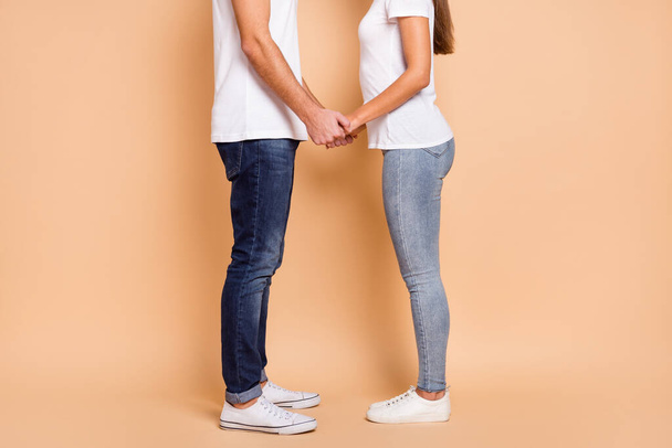 Cropped photo of married couple dressed white t-shirts jeans sneakers holding hands isolated beige color background - Foto, Bild