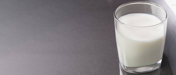 Selektywny widok góry ostrości na przezroczystą szklankę mleka na tle czarnego marmuru stołowego z przestrzenią do kopiowania, po lewej stronie. Format banera produktu mlecznego. - Zdjęcie, obraz